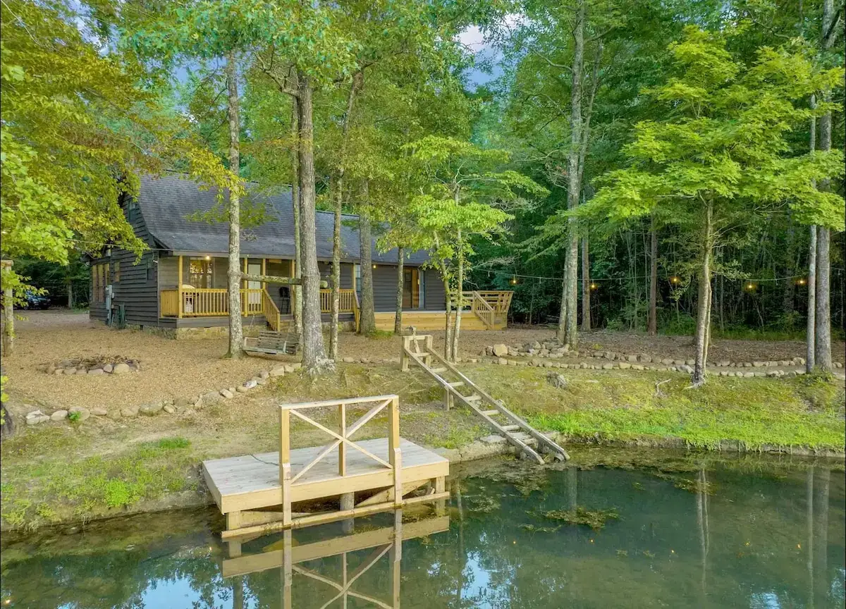 Dark-sided cabin among trees with a small wooden dock on the water in Marion County, Tennessee