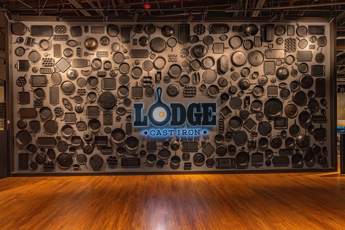 Wall of cast iron cookware around the glowing Lodge logo